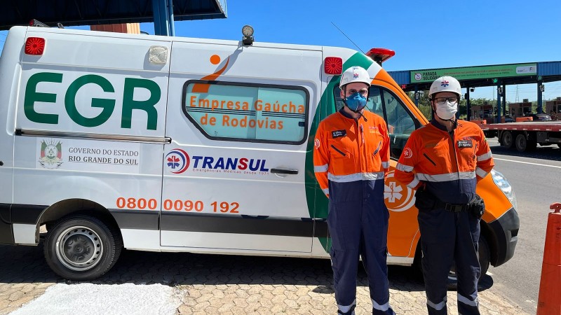 Dois socorristas posam para foto em frente à uma ambulância