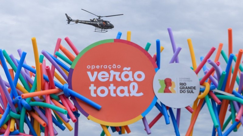 helicoptero preto voando sobre pórtico da Operação Verão Total do governo do RS