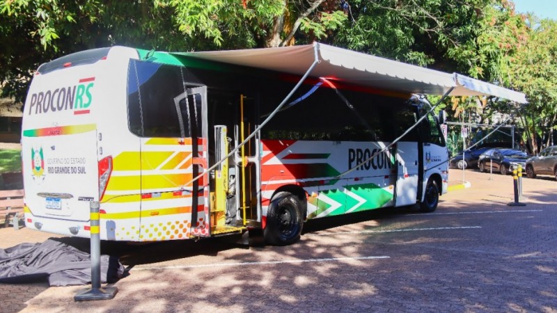 Foto horizontal mostra a lateral e a traseira de um &ocirc;nibus. Na parte de tr&aacute;s do ve&iacute;culo, l&ecirc;-se PROCONRS e, abaixo, depois de uma linha horizontal nas cores verde, vermelha e amarela, l&ecirc;-se Governo do Estado do Rio Grande do Sul ao lado direito do bras&atilde;o do Executivo. As portas do &ocirc;nibus est&atilde;o abertas e a lateral do ve&iacute;culo tamb&eacute;m traz as cores da bandeira do Rio Grande do Sul.