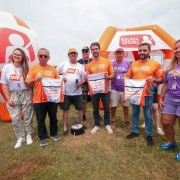 Aqui est&aacute; a descri&ccedil;&atilde;o detalhada da imagem para fins de acessibilidade: A imagem registra um evento institucional realizado em um gramado ao ar livre sob c&eacute;u nublado, com a presen&ccedil;a de autoridades do governo do Rio Grande do Sul. Figuras Centrais e A&ccedil;&atilde;o: No centro da composi&ccedil;&atilde;o, um grupo de oito pessoas posa para a foto. O governador Eduardo Leite e o vice-governador Gabriel Souza, acompanhados de um terceiro homem, seguram &agrave; frente do corpo mochilas do tipo saco de cor branca. Nas mochilas, l&ecirc;-se em destaque a frase: "Na estrada, o salva-vidas &eacute; voc&ecirc;.". Vestimentas e Identidade Visual: * Eduardo Leite e Gabriel Souza vestem camisetas laranjas com o logotipo da campanha "Ver&atilde;o Total". Outros integrantes do grupo usam camisetas roxas, tamb&eacute;m com a marca do "Ver&atilde;o Total", ou camisetas brancas com o logo da "Balada Segura". Elementos de Fundo: * &Agrave; esquerda, h&aacute; um grande infl&aacute;vel em formato esf&eacute;rico (semelhante a um capacete ou bal&atilde;o), nas cores laranja e branco, exibindo a marca "BALADA SEGURA" e o &iacute;cone de uma pessoa com cinto de seguran&ccedil;a. Ao fundo, uma estrutura infl&aacute;vel laranja em formato de tenda tamb&eacute;m exibe o logotipo da "Balada Segura". Uma parte de um ve&iacute;culo branco &eacute; vis&iacute;vel na extremidade esquerda da foto.